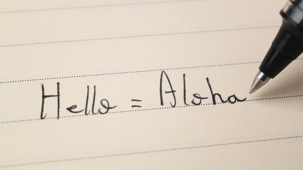 A person writing out common Hawaiian words and phrases.